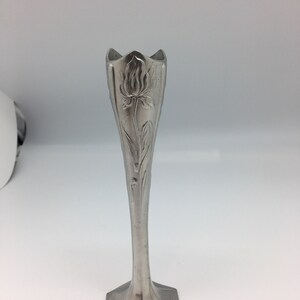 Pu&ograve; includere: Un vaso a bocciolo in stile Art Nouveau color argento. Il vaso presenta un motivo floreale sul corpo allungato e una parte superiore svasata. La base ha una forma geometrica. Il vaso &egrave; in metallo e viene presentato su sfondo bianco.