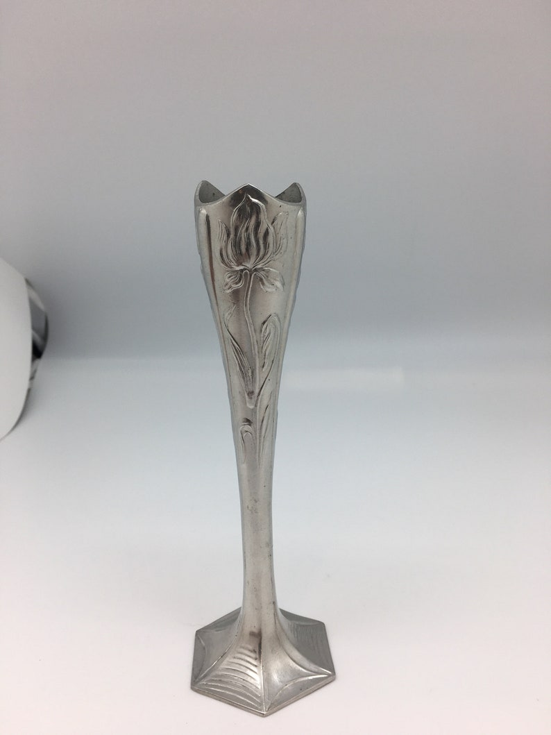Pu&ograve; includere: Un vaso a bocciolo in stile Art Nouveau color argento. Il vaso presenta un motivo floreale sul corpo allungato e una parte superiore svasata. La base ha una forma geometrica. Il vaso &egrave; in metallo e viene presentato su sfondo bianco.