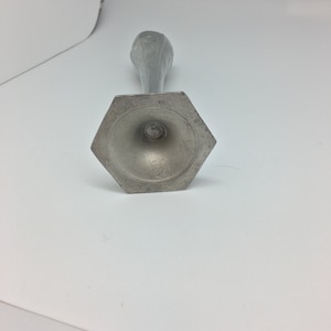 Pu&ograve; includere: Un portacandele color argento con base esagonale e stelo sottile. La parte superiore del supporto presenta un motivo floreale. Il portacandele &egrave; in metallo e si trova su una superficie bianca.