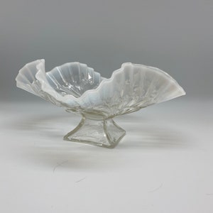 May include: A white, footed glass bowl with a ruffled rim. The bowl is made of clear glass with a frosted finish.
