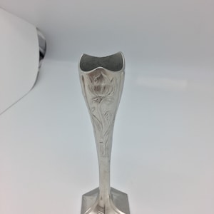 Pu&ograve; includere: Un vaso portafiori argentato con base esagonale e stelo sottile. Il vaso presenta un motivo floreale e una parte superiore svasata. Il vaso &egrave; in metallo ed &egrave; progettato per un singolo fiore.