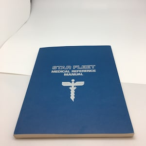 May include: A blue book with the title "STAR FLEET MEDICAL REFERENCE MANUAL" and a white medical symbol.
