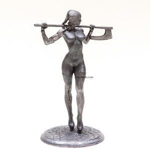 Puede incluir: Una figura de metal de color plateado de una mujer sosteniendo un hacha sobre su hombro. Lleva un liguero y medias. La figura está de pie sobre una base circular.