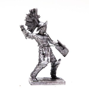K&ouml;nnte beinhalten: Eine silberfarbene Metallfigur eines r&ouml;mischen Gladiators, der einen Helm mit Federkamm tr&auml;gt und ein Schwert und einen Schild h&auml;lt.