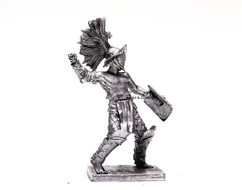 K&ouml;nnte beinhalten: Eine silberfarbene Metallfigur eines r&ouml;mischen Gladiators, der einen Helm mit Federkamm tr&auml;gt und ein Schwert und einen Schild h&auml;lt.