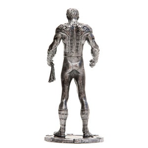 Puede incluir: Una figura plateada de Spider-Man, vista desde atr&aacute;s. La figura est&aacute; de pie sobre una base rectangular, sosteniendo una telara&ntilde;a en una mano. Los detalles del traje, incluido el patr&oacute;n de telara&ntilde;a en la espalda, son claramente visibles.
