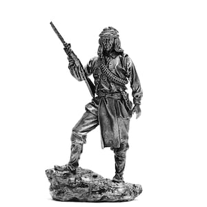 Op de afbeelding: Een zilverkleurig beeldje van een soldaat met een tulband die een geweer vasthoudt. De soldaat staat op een rotsachtige basis.