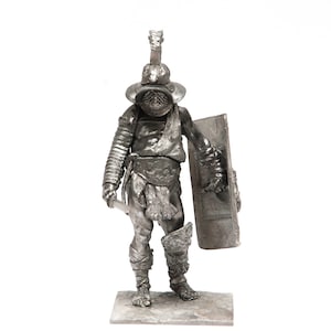 Puede incluir: Una figura de metal plateado de un gladiador romano con casco, espada y escudo.