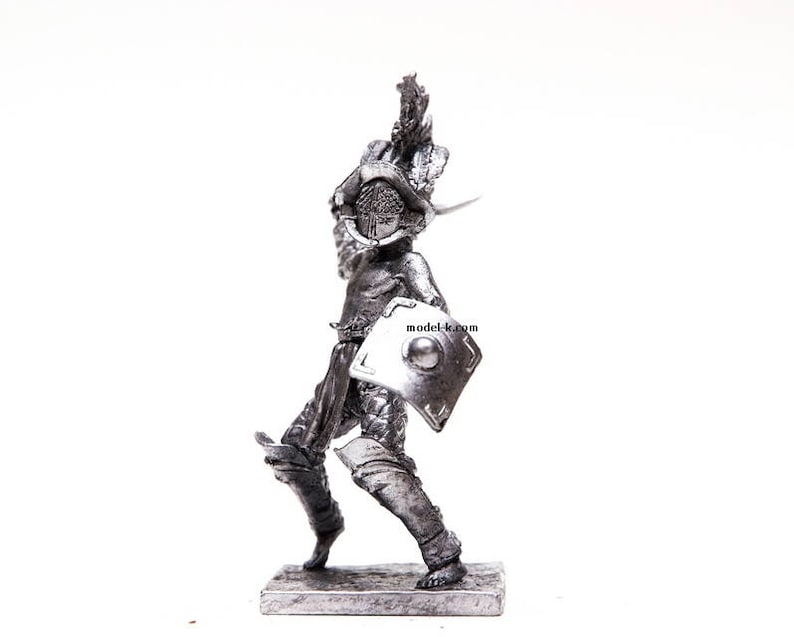 K&ouml;nnte beinhalten: Eine silberfarbene Metallfigur eines r&ouml;mischen Gladiators, der einen Schild und ein Schwert h&auml;lt. Der Gladiator tr&auml;gt einen Helm und eine R&uuml;stung. Die Figur steht auf einem kleinen Sockel.