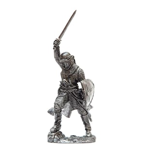 May include: A silver metal figurine of a medieval knight in armor, holding a sword and shield. The knight is wearing a helmet with a visor and a chainmail tunic. The figurine is standing on a small base.