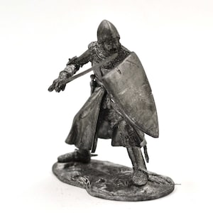 May include: A pewter figurine of a medieval knight in armor, holding a sword and shield. The knight is wearing a helmet and chainmail, and is standing on a base.