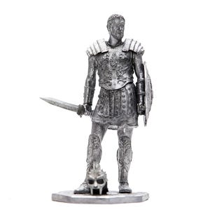Puede incluir: Una figura de plata de un soldado romano con armadura y sosteniendo una espada y un escudo. El soldado está de pie sobre una base con una calavera a sus pies.