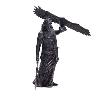 May include: A black and silver statue of a man holding an eagle. The man is wearing a robe and has a beard. The eagle is perched on his arm.