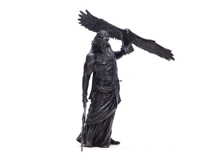 May include: A black and silver statue of a man holding an eagle. The man is wearing a robe and has a beard. The eagle is perched on his arm.