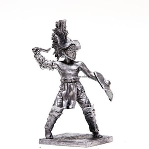 K&ouml;nnte beinhalten: Eine silberfarbene Metallfigur eines r&ouml;mischen Gladiators, der ein Schwert und einen Schild h&auml;lt. Der Gladiator tr&auml;gt einen Helm und eine R&uuml;stung.