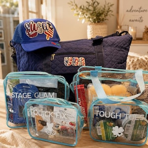 Puede incluir: Un conjunto de accesorios de viaje, que incluye una bolsa de lona azul marino, una gorra de béisbol y varias bolsas transparentes con cremallera. La gorra y la bolsa presentan diseños de "USA". Las bolsas están etiquetadas como "STAGE GLAM", "QUICK FIX" y "TOUGH TOES".