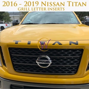 May include: A yellow 2016-2019 Nissan Titan pickup truck with black "TITAN" lettering on the front grille.