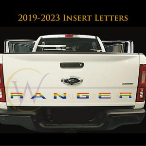 May include: The rear view of a white Ford Ranger pickup truck featuring the text 2019-2023 INSERT LETTERS at the top. The tailgate displays the word RANGER in individual letters with a horizontal rainbow gradient pattern across each character.