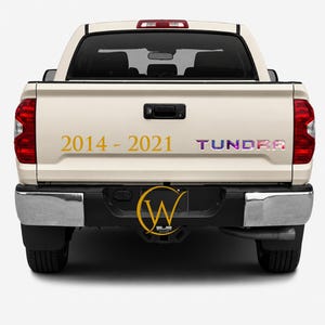 May include: A light-colored pickup truck viewed from the rear, featuring a gold-colored decal that reads 2014 - 2021 and a multi-colored, patterned decal that reads TUNDRA. A circular logo with the letters W and C is centered on the bumper.