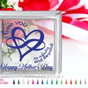 May include: A clear glass block with a blue infinity heart design and the words "I love you to infinity and beyond" and "Happy Mother's Day". The block is filled with flowers and has a white and red ribbon in the background.
