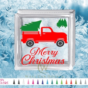 May include: Red pickup truck with a Christmas tree in the bed, driving through a snowy forest. The truck has the words "Merry Christmas" written on the side.