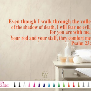 May include: A white bathroom wall with a beige tile pattern. A wall decal with the text "Even though I walk through the valley of the shadow of death, I will fear no evil, for you are with me. Your rod and your staff, they comfort me. Psalm 23:4" in orange. The decal is above a white bathroom vanity with a white countertop. There are white towels, a white soap dispenser, and a white ceramic container on the countertop.