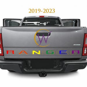 May include: A gray pickup truck tailgate featuring the text 2019-2023 at the top. The word RANGER is displayed in large, multi-colored block letters across the center, with each letter featuring a different color including red, orange, yellow, green, blue, and purple.