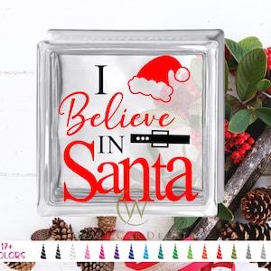 May include: A glass block with a red and black vinyl decal that says "I Believe in Santa" with a Santa hat on top of the "I".