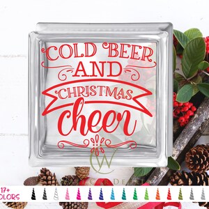 May include: A clear glass block with the words "COLD BEER AND CHRISTMAS cheer" in red script. The block is decorated with festive greenery, red berries, and pine cones, suggesting a holiday theme.