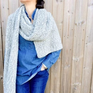 May include: A woman wearing a grey knitted scarf over a blue denim shirt and blue jeans.