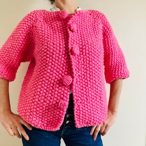 May include: A pink knitted cardigan with a button closure and short sleeves.