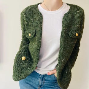Puede incluir: Un cárdigan de punto verde tweed con botones dorados. El cárdigan tiene un corte holgado y una longitud ligeramente recortada.