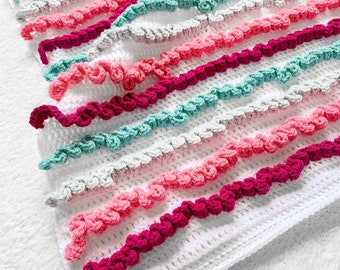 May include: A white crocheted baby blanket with pink, teal, and magenta ruffled trim.