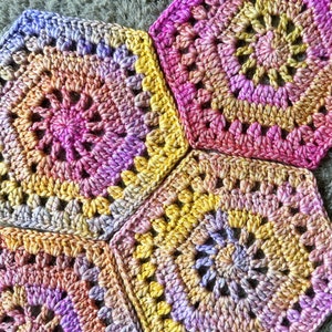 May include: Four crocheted granny squares in shades of pink, purple, yellow, and white. The squares are joined together to create a larger piece of fabric.