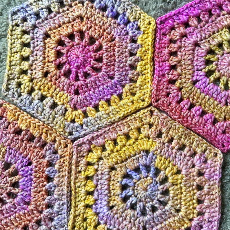 May include: Three crocheted granny squares in shades of pink, yellow, and purple. The squares are joined together to form a larger piece of fabric.