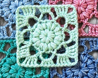 May include: Close-up of a handmade crochet square in shades of mint green, surrounded by other squares in blue and pink. The central square features a floral design with openwork details, showcasing the texture of the yarn. The overall theme is handmade crafts.