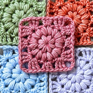 May include: Close-up of colorful crochet squares in shades of pink, green, orange, blue, and purple. Each square features a floral design with raised, textured stitches, creating a three-dimensional effect. The squares are joined together, showcasing the intricate craftsmanship.