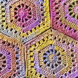 May include: Close-up of a crocheted blanket with a repeating pattern of hexagons in shades of pink, purple, yellow, and orange.
