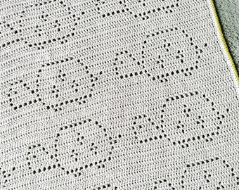 May include: Close-up of a white crocheted blanket with a repeating heart pattern. The blanket is made of a soft, textured yarn and has a delicate, openwork design. The edges are finished with a yellow border.