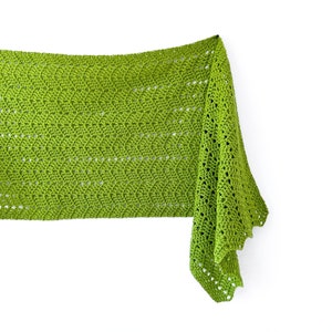 May include: A lime green crochet shawl with a scalloped edge. The shawl is draped over a white background.