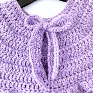 May include: A purple crocheted shawl with a tied bow at the neck.