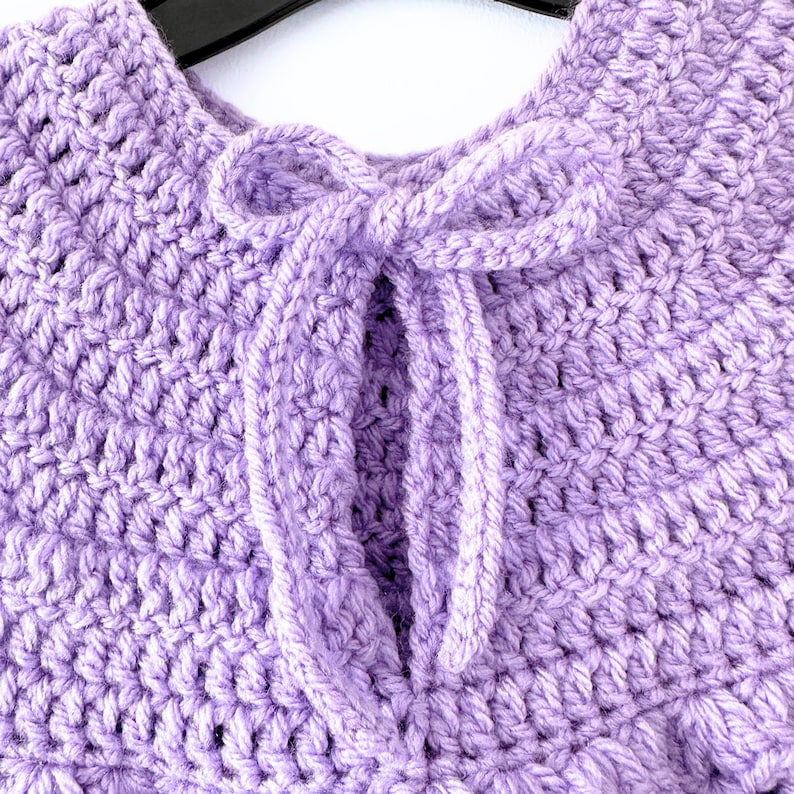 May include: A purple crocheted shawl with a tied bow at the neck.