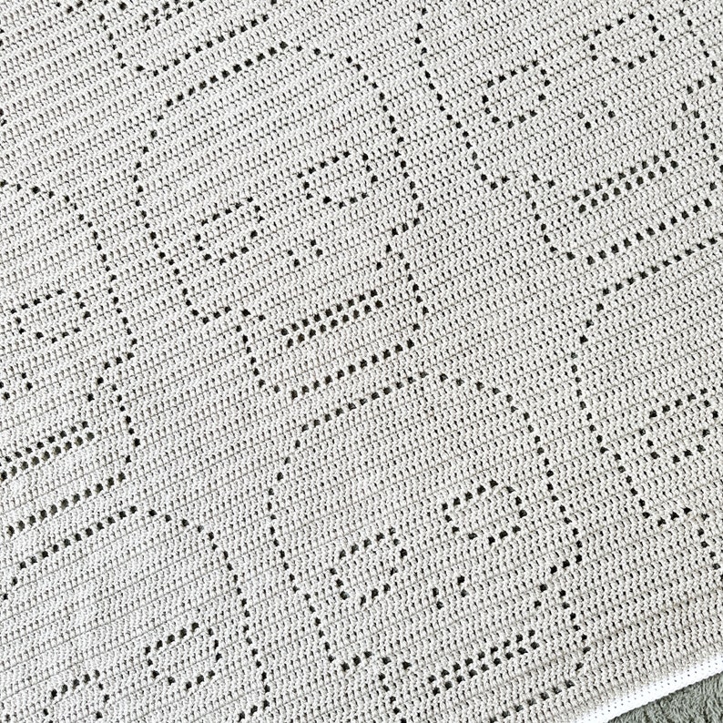 Pu&ograve; includere: Primo piano di una coperta all'uncinetto con un motivo a rombi di colore grigio chiaro.
