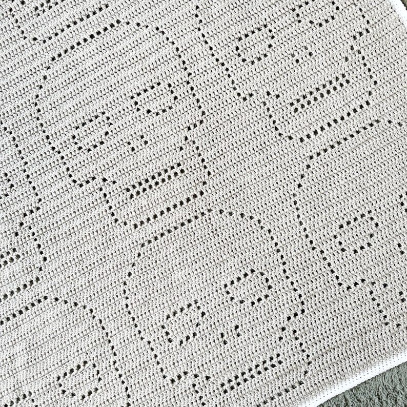 Pu&ograve; includere: Primo piano di una copertina per neonati all'uncinetto con un motivo a rombi di colore grigio chiaro.