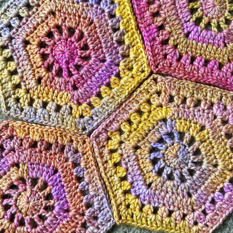 May include: Close-up of a crocheted blanket made of colorful squares in shades of pink, yellow, and orange.