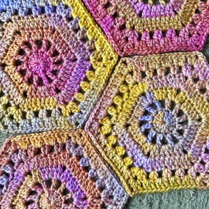 May include: A close-up of a crocheted blanket with a multi-colored granny square pattern in shades of pink, purple, yellow, and orange.
