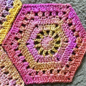 May include: A close-up of a crocheted hexagon with a gradient of pink, yellow, and orange yarn.