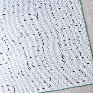 May include: White crochet blanket with a geometric pattern of black outlined shapes. The blanket has a green border.