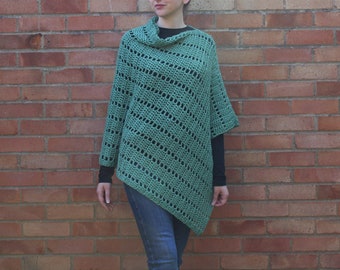 Op de afbeelding: Een groene gehaakte poncho met een rolkraag en een diagonaal patroon. De poncho wordt gedragen over een zwart longsleeve shirt en een blauwe jeans.