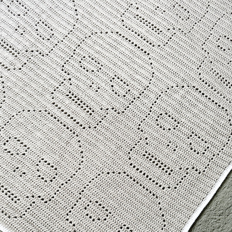 Pu&ograve; includere: Una coperta all'uncinetto bianca con un motivo geometrico. La coperta ha un bordo bianco.